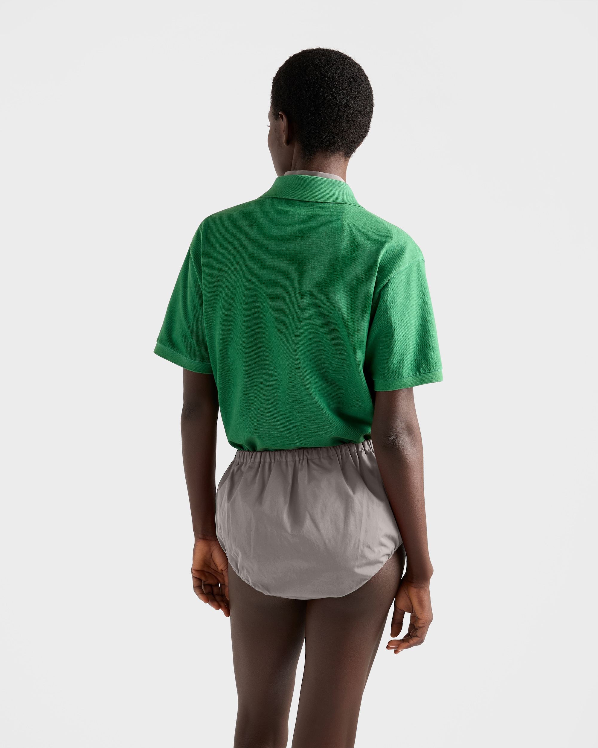 Model wearing green piqué polo shirt from the back.